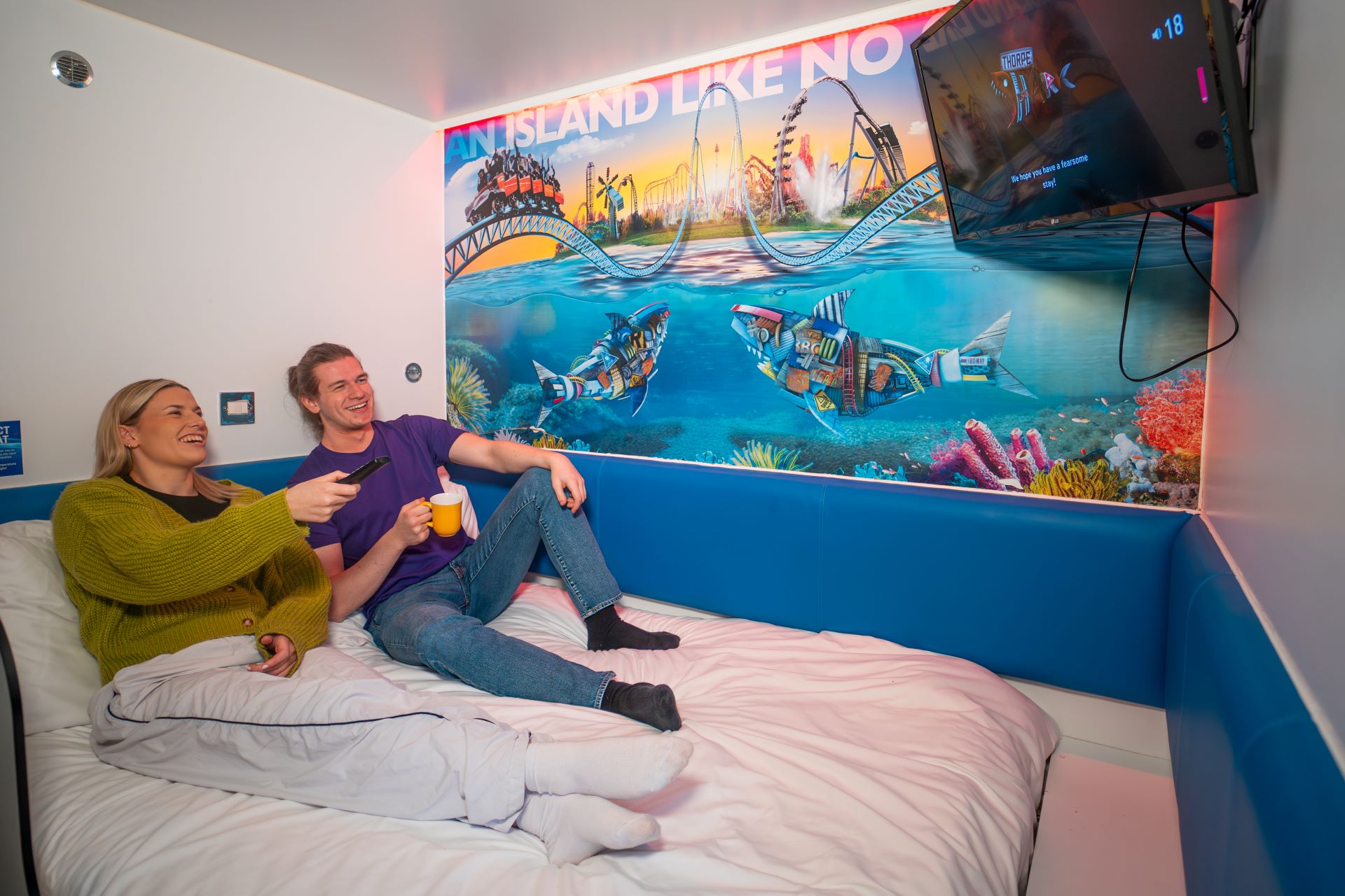 Guests sat on top of the bed watching the Tv in a Thorpe Shark Cabin