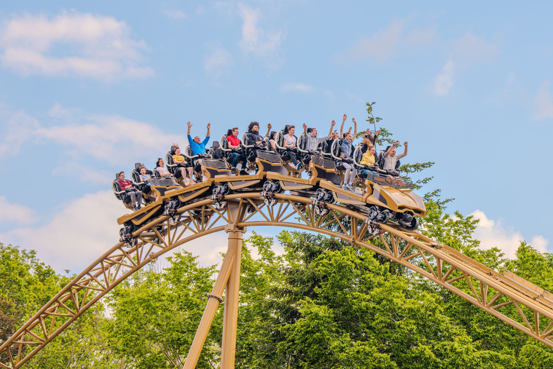 Hyperia: Full train of guests riding Hyperia on the track with a blue sky and trees in the background